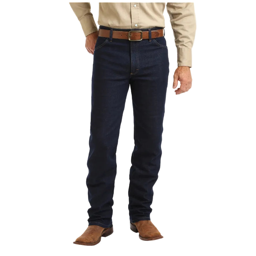 A person stands against a white background, showing only their lower half wearing Wrangler Mens Cowboy Cut Active Flex Jeans (13MAFPW36) in Prewashed Indigo. They're also dressed in a beige shirt, brown belt, and brown cowboy boots.