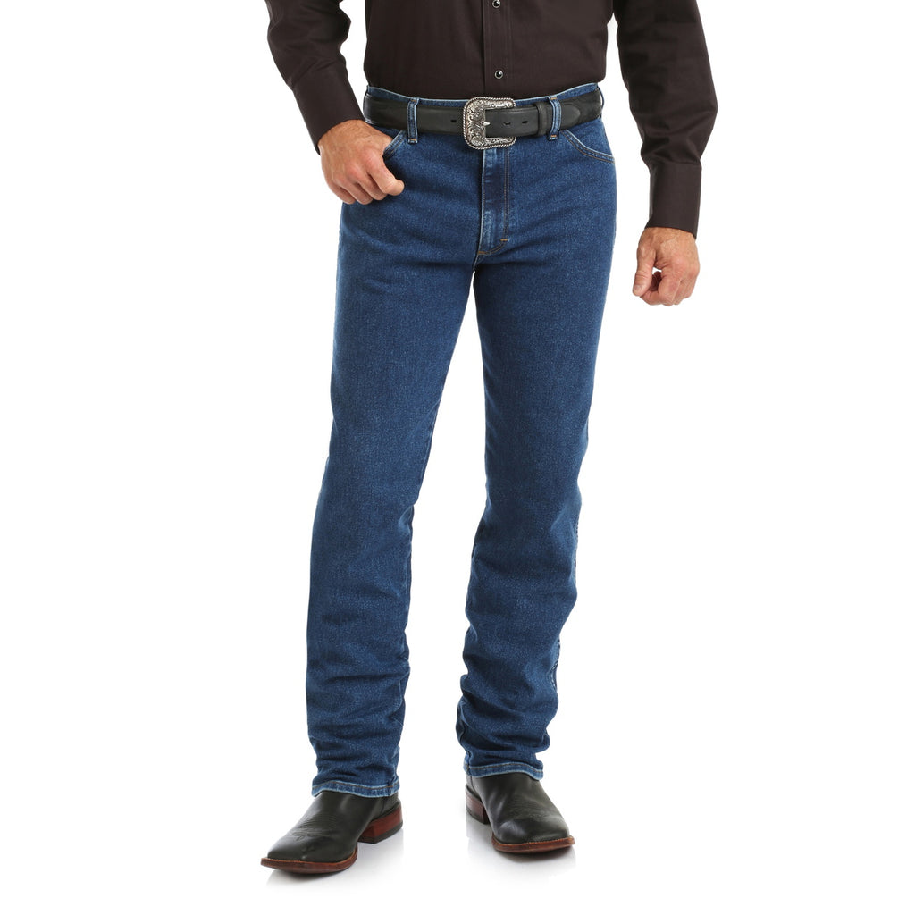 A person in a black long-sleeve shirt, Wrangler Men's Cowboy Cut Original Fit Active Flex Jeans (13MAFGK34) Stonewash, a black belt with a large buckle, and black cowboy boots stands against a white background. Head not visible.