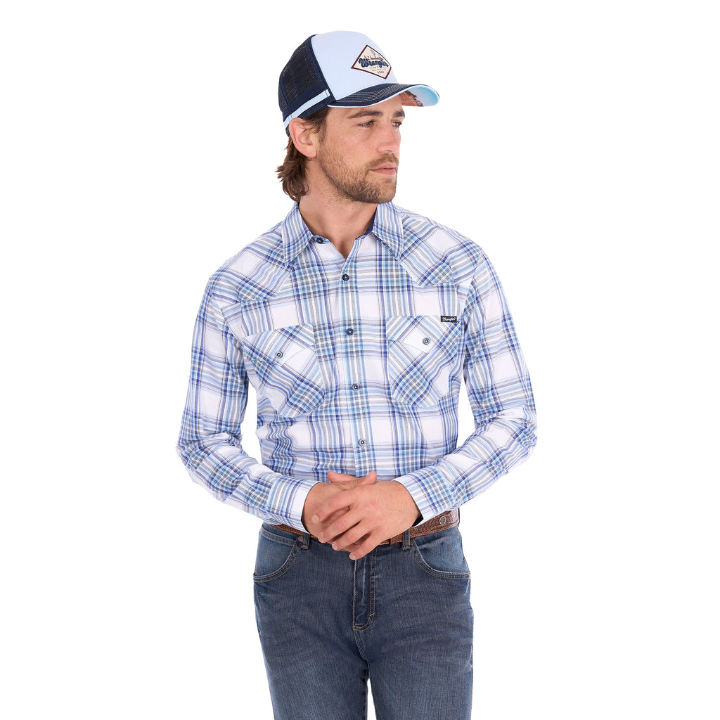 A man wearing a light blue, royal blue and white Wrangler Men's Eric long-sleeve western-style plaid button-down Shirt (X6S1111667) paired with dark blue jeans and a matching Wrangler Hank High Profile Trucker Cap (X6S1943CAP), set against a plain white background.