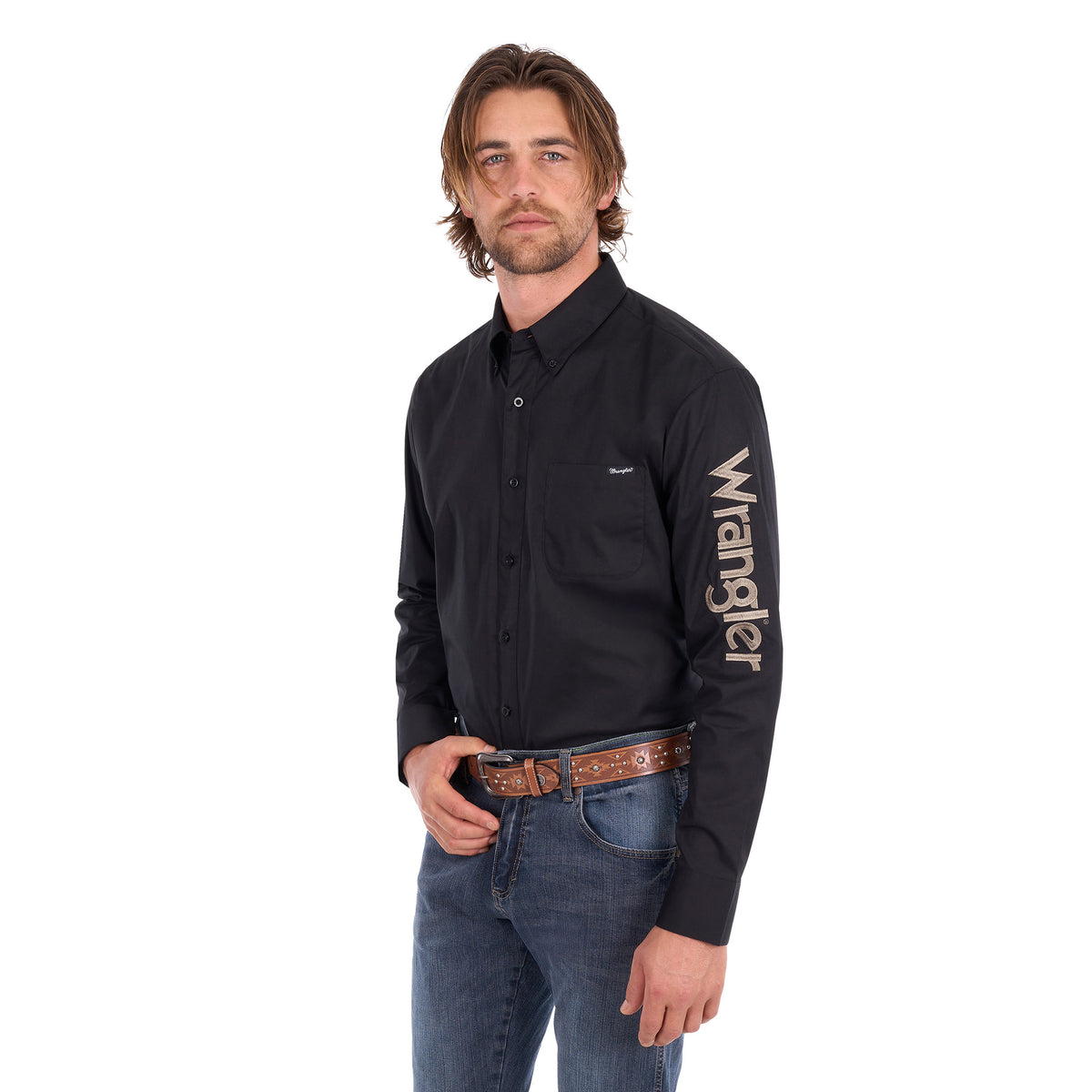 A man wearing a black Wrangler Men's Flex Logo Long Sleeve Shirt (XCP1155359) with a light tan Wrangler Onyx Belt (X6S1969BLT) and blue jeans, standing against a solid white background.
