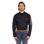 A man wearing a black Wrangler Men's Flex Logo Long Sleeve Shirt (XCP1155359) with a light tan Wrangler Onyx Belt (X6S1969BLT) and blue jeans, standing against a solid white background.