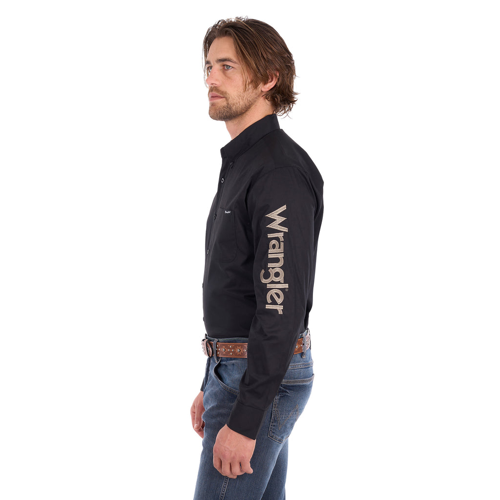 A man in profile wearing a black Wrangler Men's Flex Logo Long Sleeve Shirt (XCP1155359) with a light tan Wrangler Onyx Belt (X6S1969BLT) and blue jeans, standing against a solid white background.