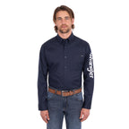 A man wearing a navy blue Wrangler Men's Flex Logo Long Sleeve Shirt (XCP1155359) with a white logo printed vertically on the left sleeve, paired with blue jeans and a Wrangler Onyx Belt (X6S1969BLT), against a plain white background.