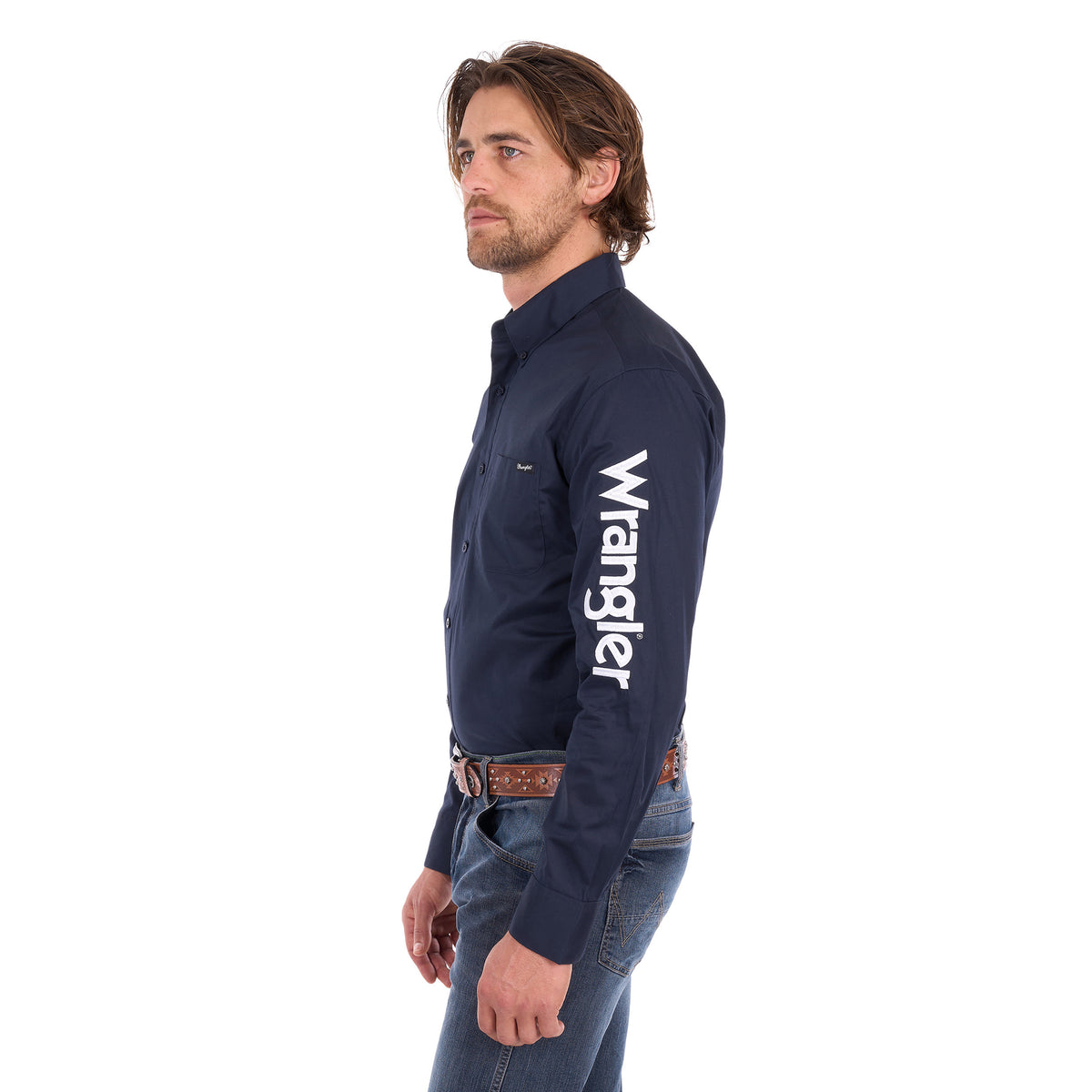 A man in profile wearing a navy blue Wrangler Men's Flex Logo Long Sleeve Shirt (XCP1155359) with a white logo printed vertically on the left sleeve, paired with blue jeans and a Wrangler Onyx Belt (X6S1969BLT), against a plain white background.