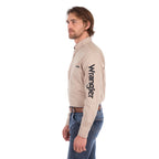 A man in profile wearing a sand Wrangler Men's Flex Logo Long Sleeve Shirt (XCP1155359) with a black logo printed vertically on the left sleeve, paired with blue jeans and a Wrangler Onyx Belt (X6S1969BLT), against a solid white background.