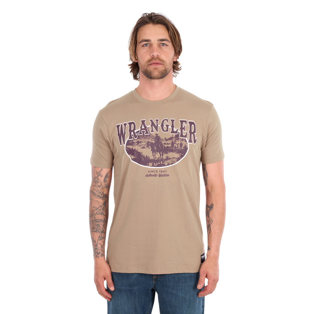 A man wearing a tan Wrangler Men's James Short Sleeve T-Shirt (XCP1557686) with a vintage-style graphic on the chest, paired with blue jeans, photographed against a solid white background.