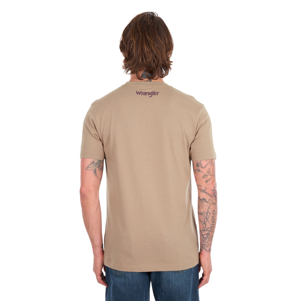 A man viewed from behind wearing a tan Wrangler Men's James Short Sleeve T-Shirt (XCP1557686) with a logo back neck print, paired with blue jeans, photographed against a solid white background.