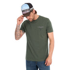 A man wearing a cypress green Wrangler Men's Jay Short Sleeve T-shirt (XCP1557683) with a small Wrangler logo on the left chest, paired with a Wrangler Evan High Profile Trucker Cap (X6S1951CAP) and blue jeans, photographed against a solid white background.
