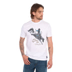 A man wearing a white Wrangler Men's Michael Short Sleeve Tee (X6S1557684) with a graphic of a cowboy riding a bucking bronco and the text 'where legendary lives' and a Wrangler logo, paired with blue jeans, against a plain white background.