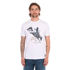 A man wearing a white Wrangler Men's Michael Short Sleeve Tee (X6S1557684) with a graphic of a cowboy riding a bucking bronco and the text 'where legendary lives' and a Wrangler logo, paired with blue jeans, against a plain white background.