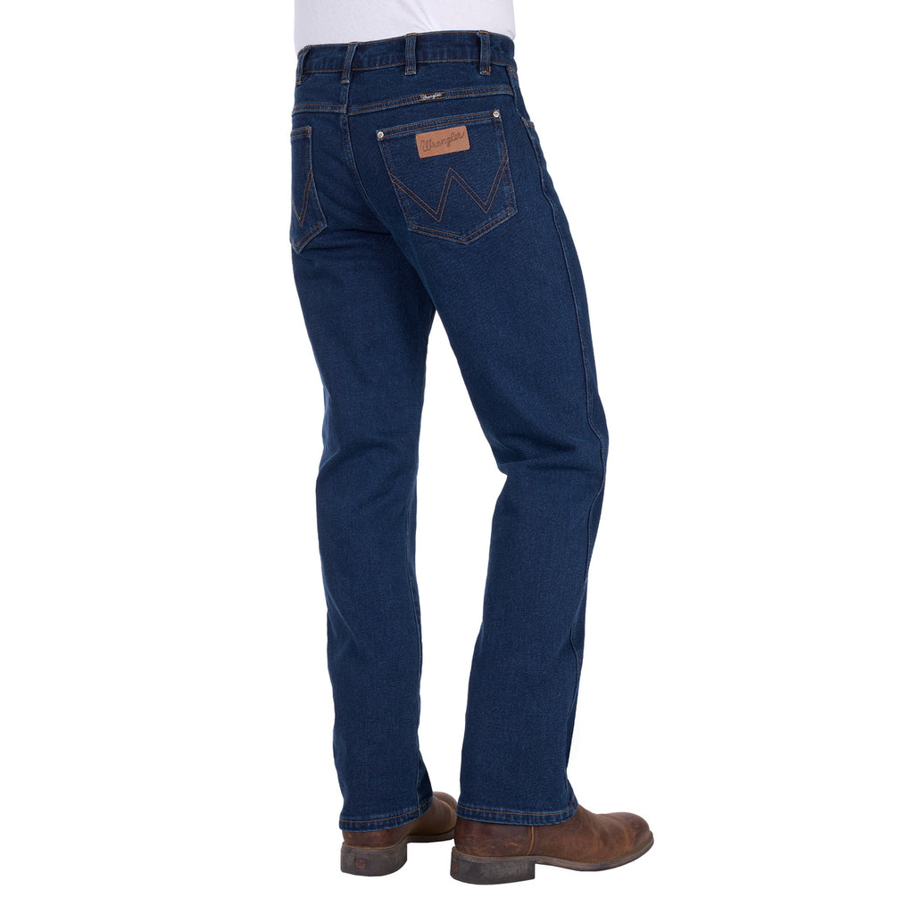 Rear three-quarter view of a man wearing a pair of original rinse dark blue Wrangler Men's Regular Bootcut Jeans (XLR1201032) with brown boots against a plain white background.