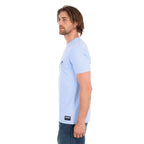A man in profile wearing a light blue Wrangler Men's Steve Short Sleeve Tee (X6S1557597) with a small circular graphic on the left chest, paired with blue jeans, photographed against a solid white background.