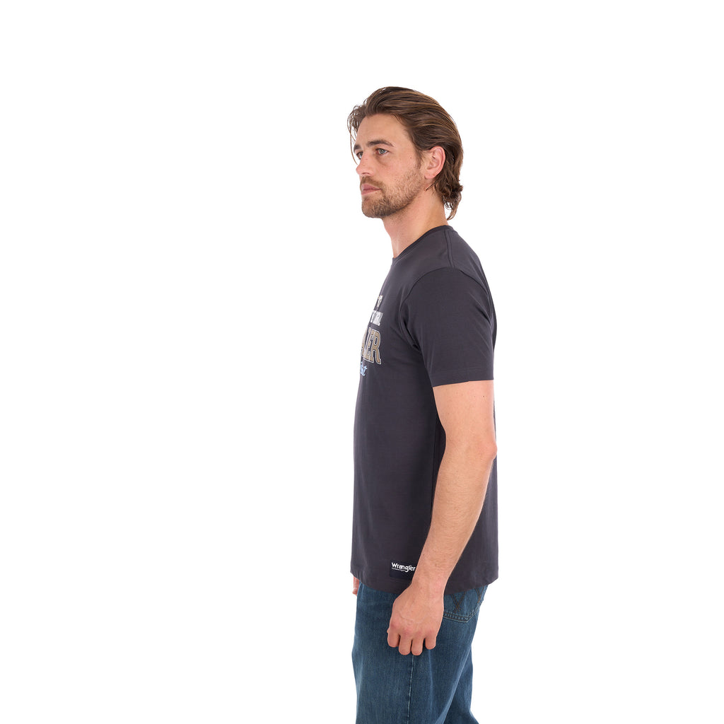 A man in profile wearing a charcoal Wrangler Men's Tim Short Sleeve Tee (X6S1557696) with a Wrangler graphic on the chest, paired with blue jeans, standing against a plain white background.