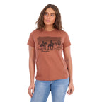 A woman wearing a copper coloured Wrangler Women's Adele S/S Tee (X6S2598644) with a dark graphic print on the front, paired with light blue jeans, against a plain white background.