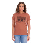 A woman wearing a copper coloured Wrangler Women's Adele S/S Tee (X6S2598644) with a dark graphic print on the front, paired with light blue jeans, against a plain white background.
