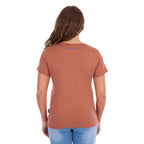 A woman wearing a copper coloured Wrangler Women's Adele S/S Tee (X6S2598644) with a Wrangler logo on the back neck, paired with light blue jeans, shown from the back against a plain white background.