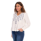 A 3-4 view of a woman modelling a white Wrangler Women's Ava Long Sleeve Blouse (X6S2501614) with vertical blue embroidered patterns on the front, paired with blue jeans, against a plain white background.