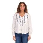 A woman modelling a white Wrangler Women's Ava Long Sleeve Blouse (X6S2501614) with vertical blue embroidered patterns on the front, paired with blue jeans, against a plain white background.
