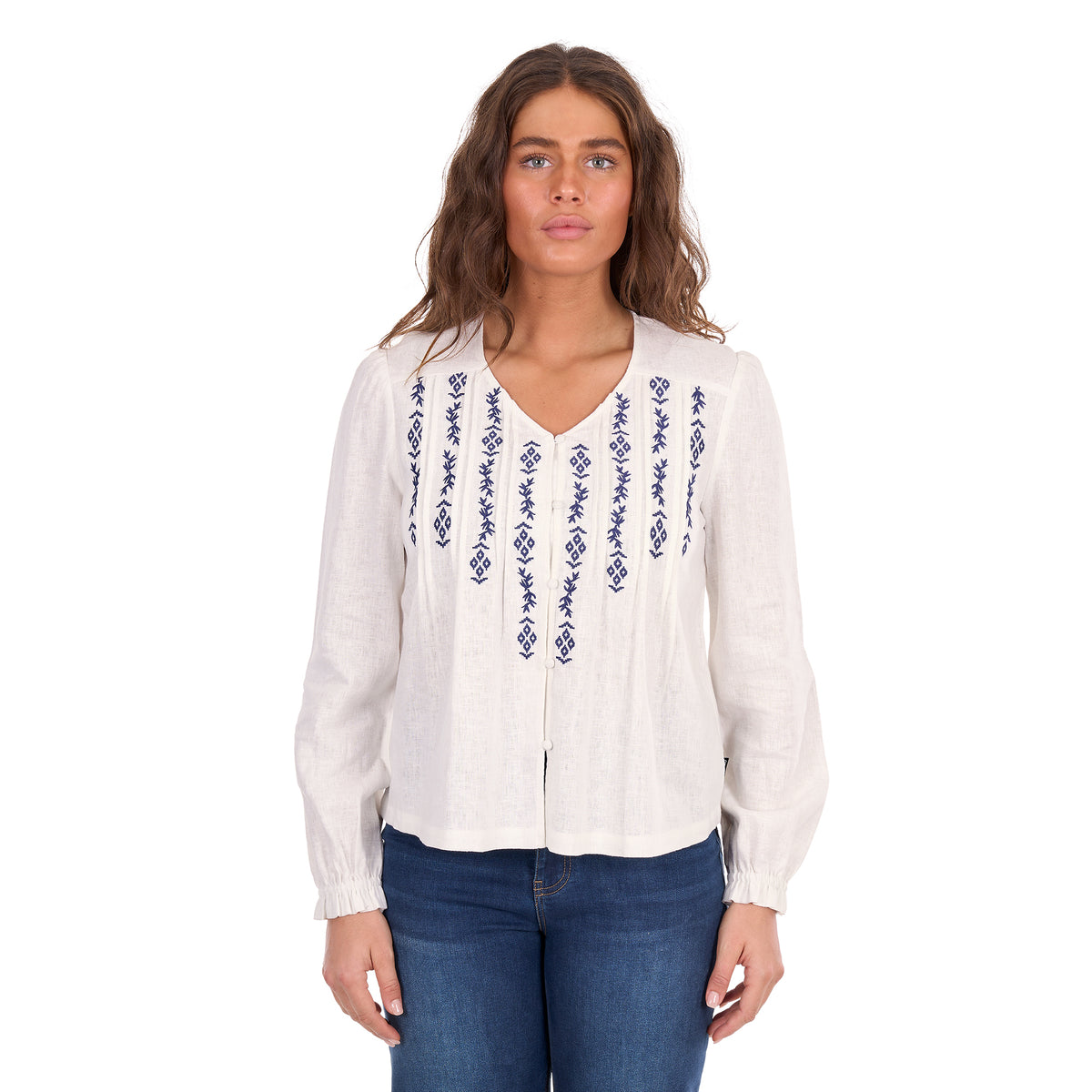 A woman modelling a white Wrangler Women's Ava Long Sleeve Blouse (X6S2501614) with vertical blue embroidered patterns on the front, paired with blue jeans, against a plain white background.