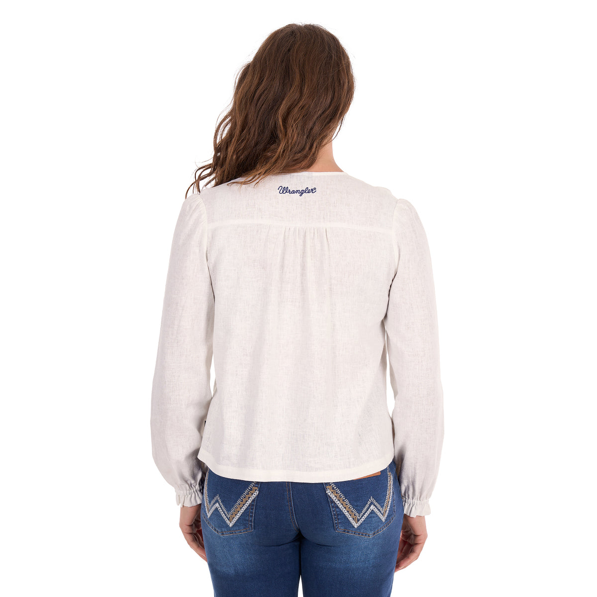 A woman viewed from behind modelling a white Wrangler Women's Ava Long Sleeve Blouse (X6S2501614) with a blue Wrangler back neck logo, paired with blue jeans, against a plain white background.