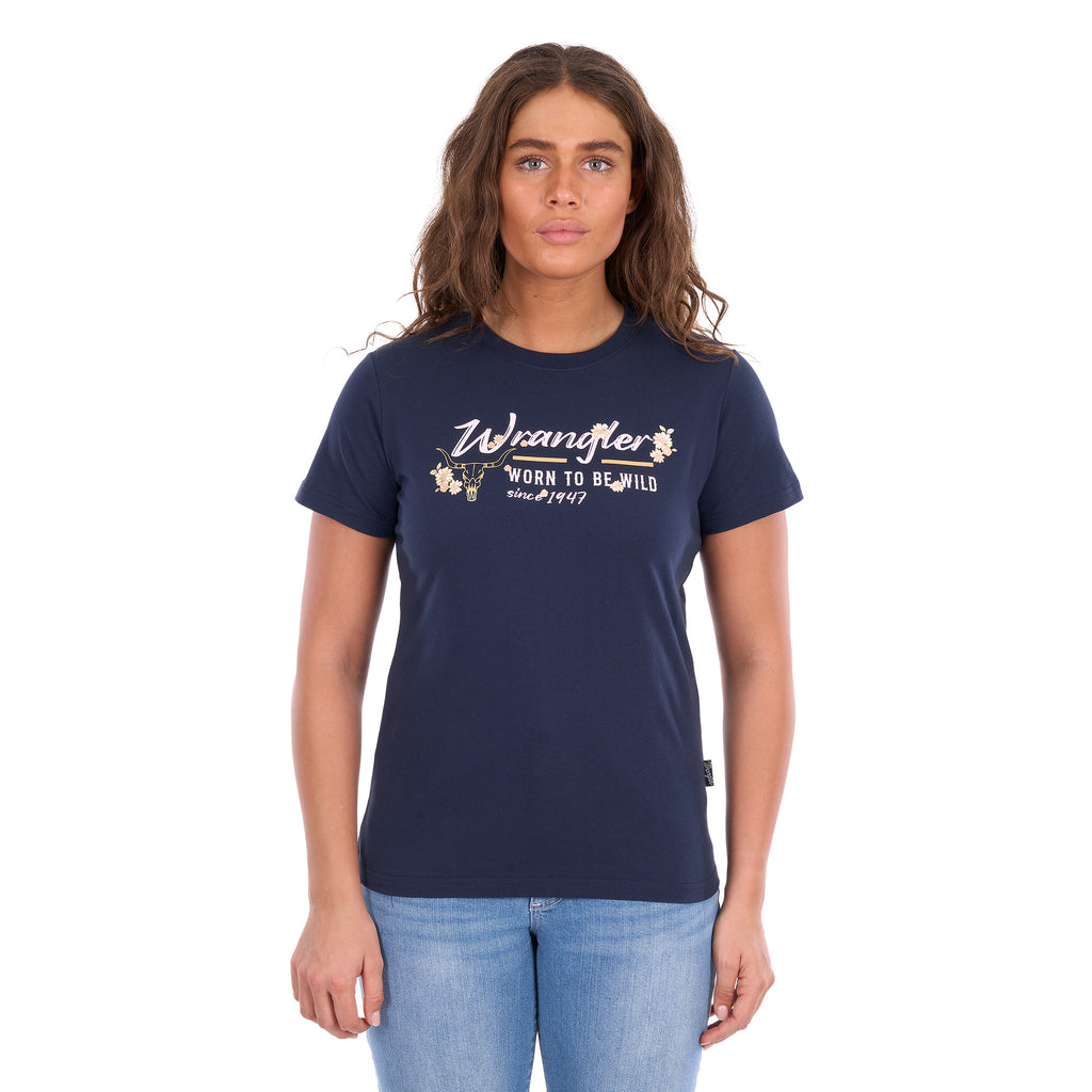 A woman modelling a navy blue Wrangler Belle Tee (X6S2598643) with a yellow and white Wrangler graphic print on the chest, paired with light blue jeans, against a plain white background.