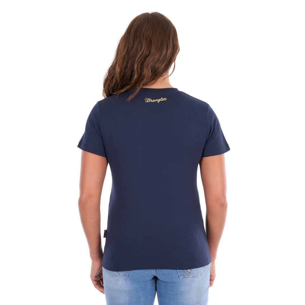 A woman viewed from behind modelling a navy blue Wrangler Belle Tee (X6S2598643) with a Wrangler logo on the back neck, paired with light blue jeans, against a plain white background.