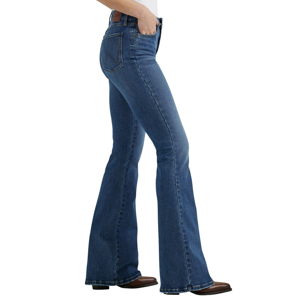 A woman shown in profile from the waist down modelling a pair of Wrangler Women's Bespoke Hi Rise Flare Jeans (112359281) paired with a white tee and brown pointed boots on a white background.