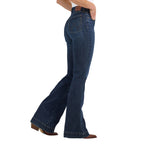 A profile view of a woman modelling a pair of Alexandra blue Wrangler Women's Bespoke Hi Rise Trouser Jeans (112367600) with a slight flare, paired with a white top and brown boots, against a plain white background.