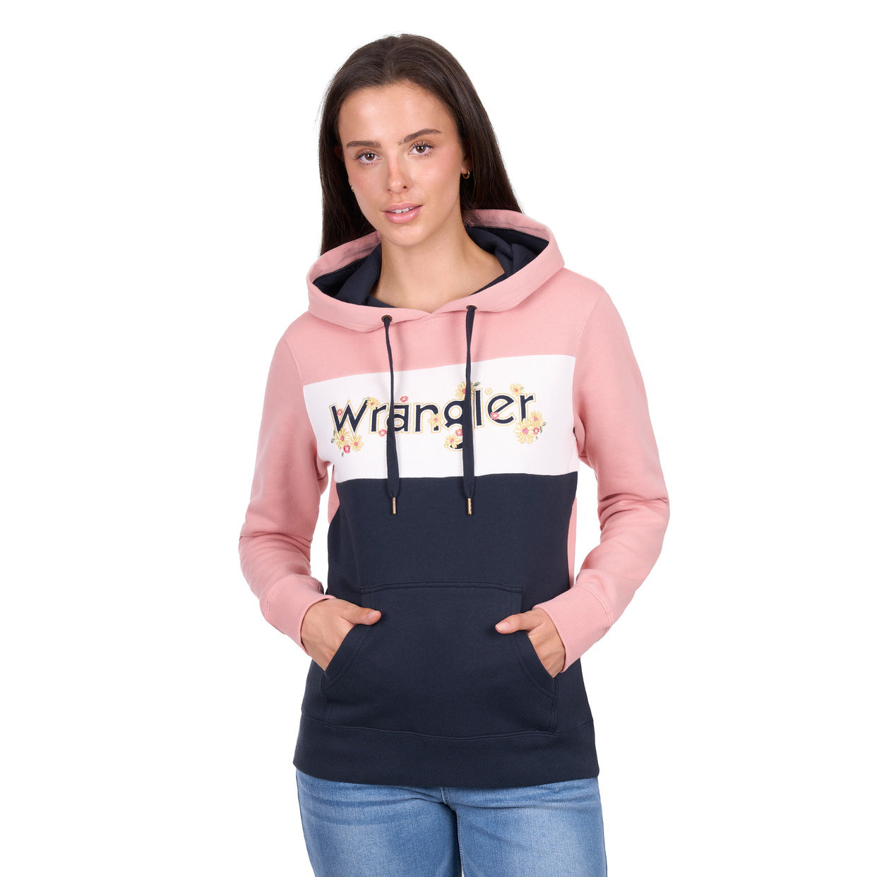 A woman wears the Wrangler Womens Brooke Hoodie (X6W2597541) in Rose/Navy—a heavyweight fleece pullover with front pocket, "wrangler" and floral embroidery on the chest—as she stands facing the camera.