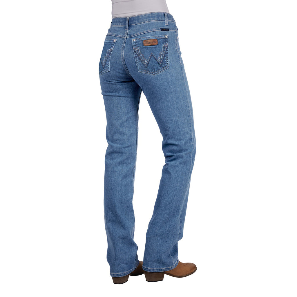Rear view of a woman wearing faded blue Wrangler Women's Chara Willow Jeans (XCP2251216) with decorative stitching on the back pockets and brown cowboy boots, shown against a plain white background.