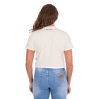 A woman viewed from behind, modelling a Wrangler Women's Cindy Crop Short Sleeve T-Shirt (XCP2596647) in cream with a navy blue 'Wrangler' rope logo across the back neck, paired with blue jeans and a tan Wrangler Western Molly Belt (XCP2919BLT), against a plain white background.