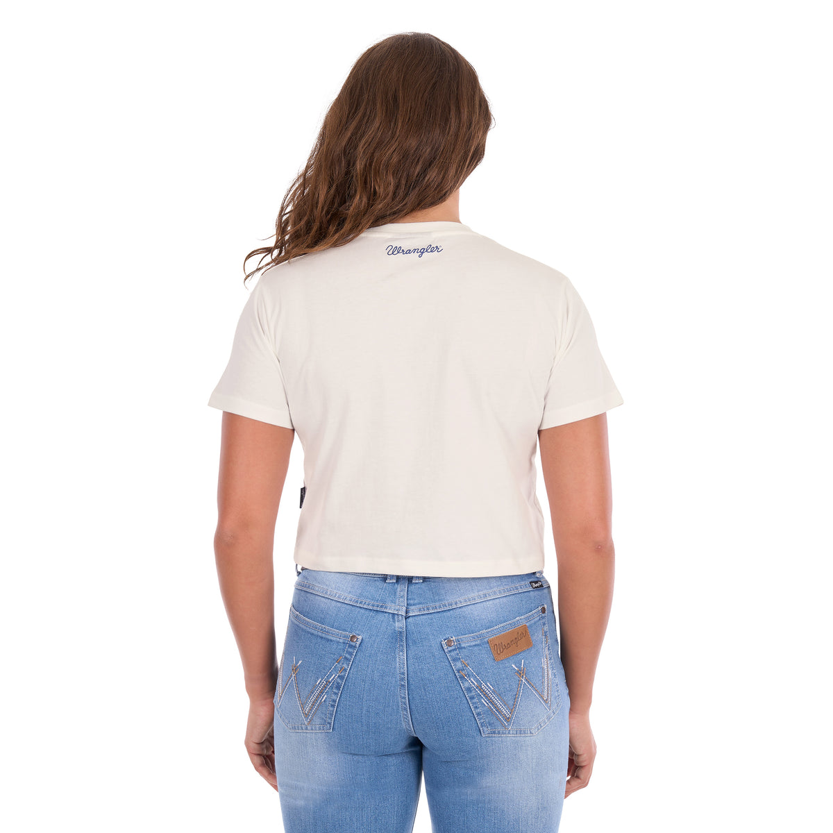 A woman viewed from behind, modelling a Wrangler Women's Cindy Crop Short Sleeve T-Shirt (XCP2596647) in cream with a navy blue 'Wrangler' rope logo across the back neck, paired with blue jeans and a tan Wrangler Western Molly Belt (XCP2919BLT), against a plain white background.