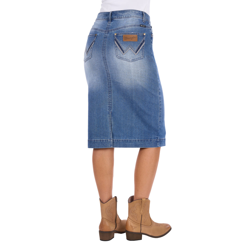 A Wrangler Women's Emmie Denim Skirt (X6S2410724) in light Kora Blue with embroidered pockets shown on a model photographed from behind, from the waist down, paired with tan cowboy boots against a plain white background.