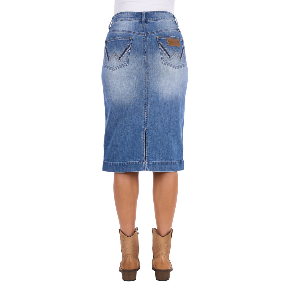 A Wrangler Women's Emmie Denim Skirt (X6S2410724) in light Kora Blue with embroidered pockets shown on a model from the waist down, from behind, paired with tan cowboy boots against a plain white background.