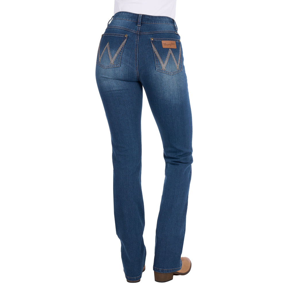 Rear view of a woman wearing mid indigo blue western-style Wrangler Women's Etta Bootcut Jeans Bailey (XCP2255711) with a white top and tan boots, shown against a plain white background.