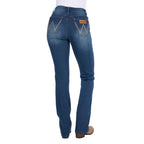 Rear view of a woman wearing mid indigo blue western-style Wrangler Women's Etta Bootcut Jeans Bailey (XCP2255711) with a white top and tan boots, shown against a plain white background.