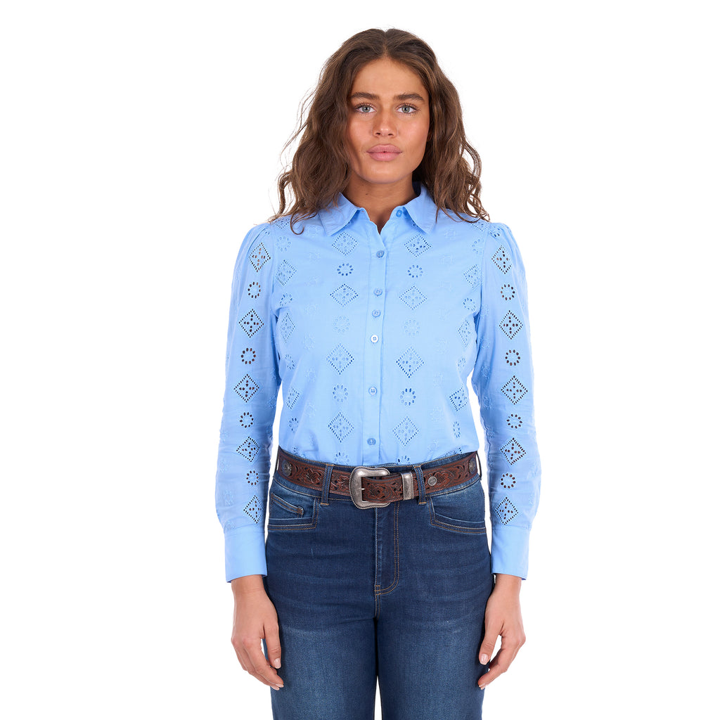 A woman modelling a cornflower blue Wrangler Women's Fleur Long Sleeve Shirt (X6S2104600) with embroidered Aztec inspired patterns, paired with dark blue jeans and a tan Wrangler Molly Belt (XCP2919BLT), against a plain white background.