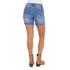 Rear view of a model wearing faded blue Wrangler Women's Gigi Mid Rise Denim Shorts (XCP2411717) with a western-style 'W' patch on the back pocket, paired with tan cowboy boots against a white background.