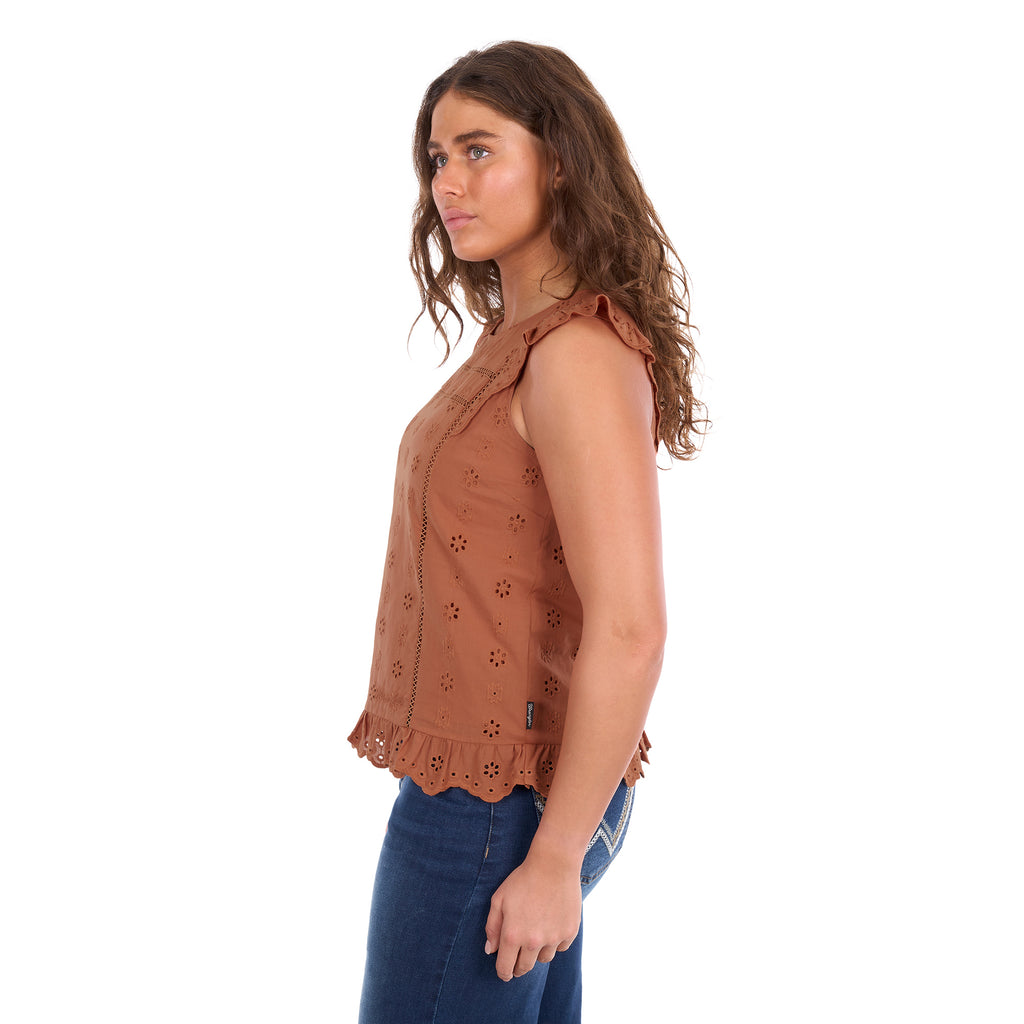 A woman viewed in profile modelling a copper Wrangler Women's Grace Sleeveless Blouse (X6S2502615) with eyelet embroidery and a ruffled hem, paired with blue jeans, against a plain white background.