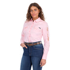 A woman modelling a blush pink Wrangler Women's Hazel Logo Long Sleeved Shirt (XCP2111608) with copper and pink Wrangler script embroidery on the right sleeve, paired with blue jeans and a brown western belt against a plain white background.