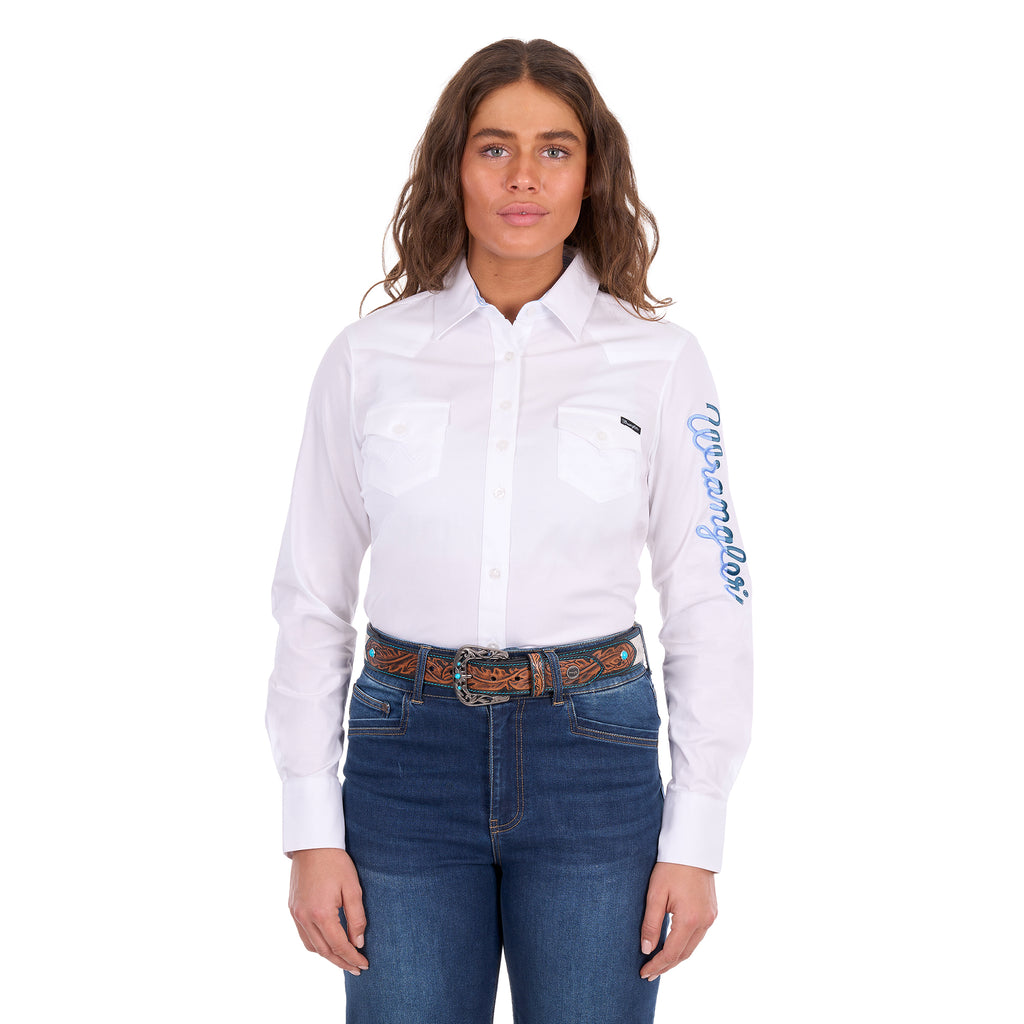 A woman modelling a white Wrangler Women's Hazel Logo Long Sleeved Shirt (XCP2111608) with blue Wrangler script embroidery on the right sleeve, paired with blue jeans and a brown western belt against a plain white background.