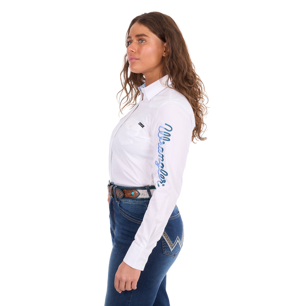 A woman modelling a white Wrangler Women's Hazel Logo Long Sleeved Shirt (XCP2111608) with blue Wrangler script embroidery on the right sleeve, paired with blue jeans and a brown western belt against a plain white background.