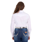 A woman modelling a white Wrangler Women's Hazel Logo Long Sleeved Shirt (XCP2111608) with blue Wrangler script embroidery on the back neck, paired with blue jeans and a western belt against a plain white background.