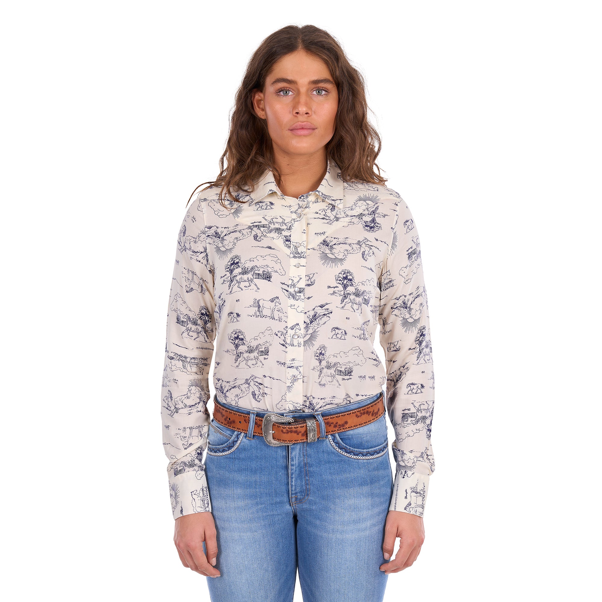 A woman modelling a cream Wrangler Women's Ivory Long Sleeve Shirt (X6S2103602) with a western novelty print paired with kora blue Wrangler Women's Margo Trouser Jeans Willow (XCP2253710) and a Wrangler Silvie Belt (X6S2920BLT), against a plain white studio background.