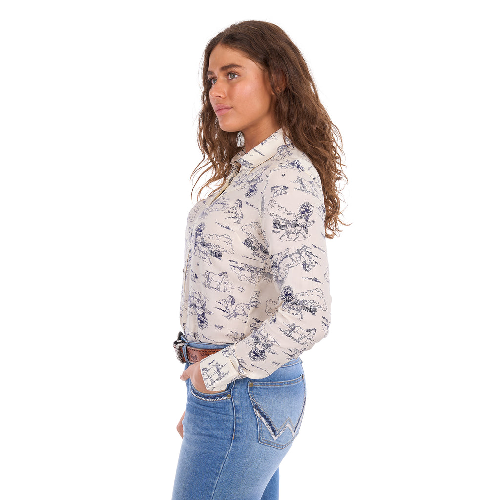 A woman in profile modelling a cream Wrangler Women's Ivory Long Sleeve Shirt (X6S2103602) with a western novelty print paired with kora blue Wrangler Women's Margo Trouser Jeans Willow (XCP2253710) and a Wrangler Silvie Belt (X6S2920BLT), against a plain white studio background.