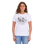 A woman modelling a white graphic Wrangler Women's Josie Short Sleeve T-Shirt (XCP2598641) with a black and white print of riders on a fence and the text 'Wrangler Butts Drive Me Nuts' on the front, paired with blue jeans against a plain white background.