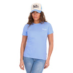 A woman facing the camera wearing a light blue crewneck Wrangler Women's Lola Short Sleeved Tee (X6S2598642) with a small white logo on the left chest, paired with a Wrangler Josie High Profile Trucker Cap (X6S2943CAP) in Cream and Light Blue, with blue jeans, against a solid white background.