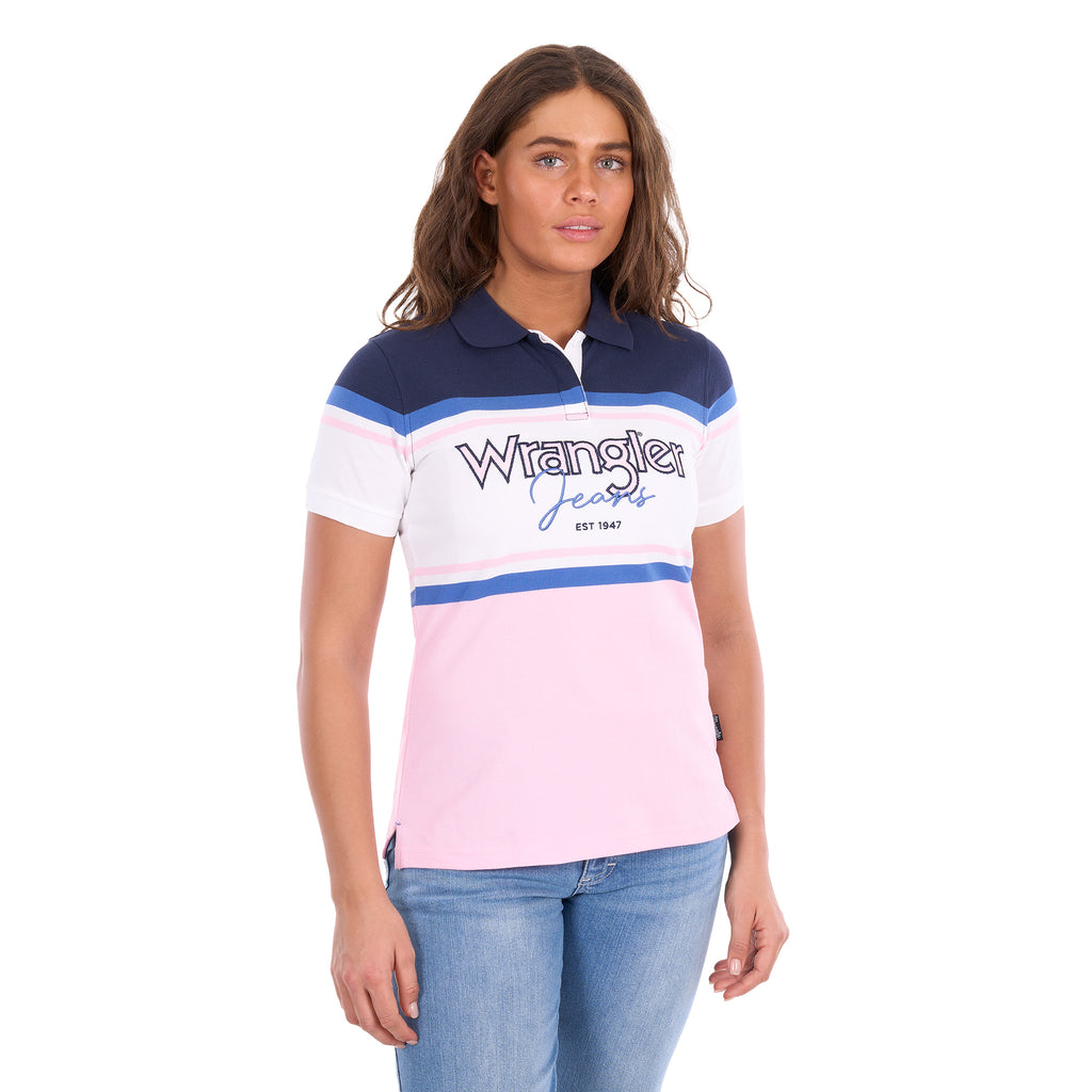 A woman modelling a Pink and Navy Wrangler Women's Maeve S/S Polo (X6S2513627) with a colour-blocked design in navy blue, white, and light pink, paired with blue jeans against a plain white background.