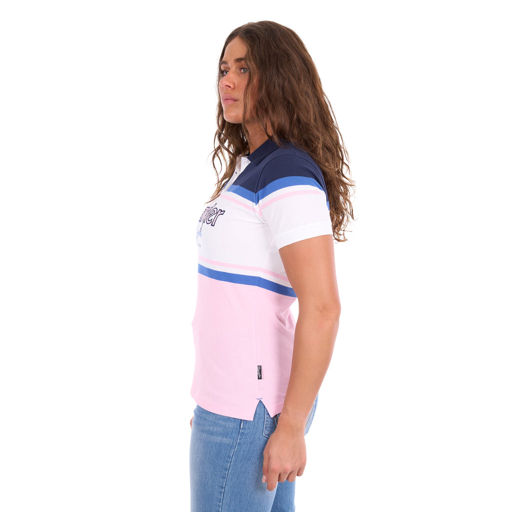 A woman modelling a Pink and Navy Wrangler Women's Maeve S/S Polo (X6S2513627) with a colour-blocked design in navy blue, white, and light pink, paired with blue jeans against a plain white background, photographed from the side.