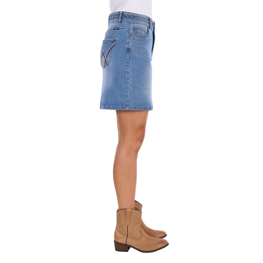 A side profile view of a faded blue Wrangler Women's Maisy Denim Skirt (XCP2409723) with decorative embroidery on the pockets, shown on a model in profile wearing tan cowboy boots against a white background.